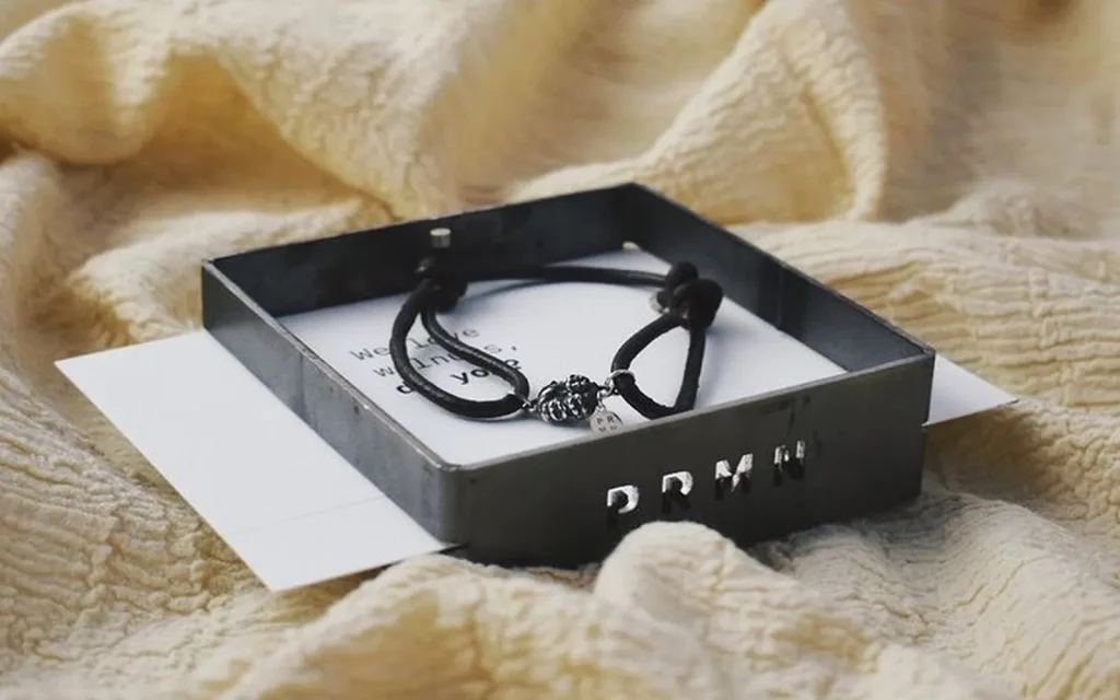 El packaging de PRMN amb la peça acabada a dins, sobre teixit clar.