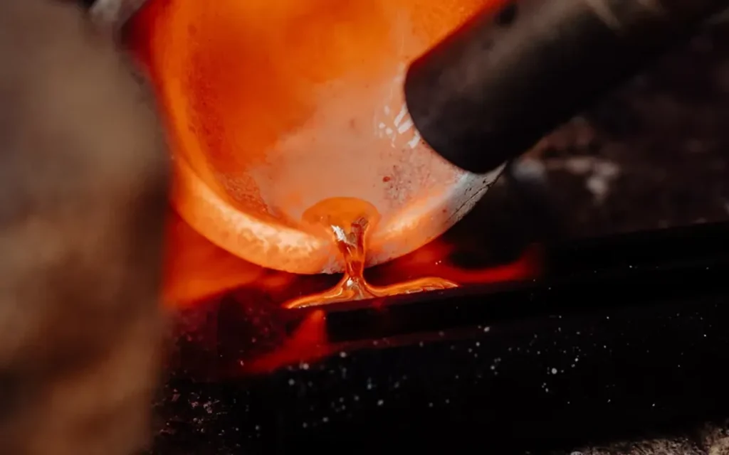 El metall fos al gresol, amb el taronja del foc contra el gris del taller.