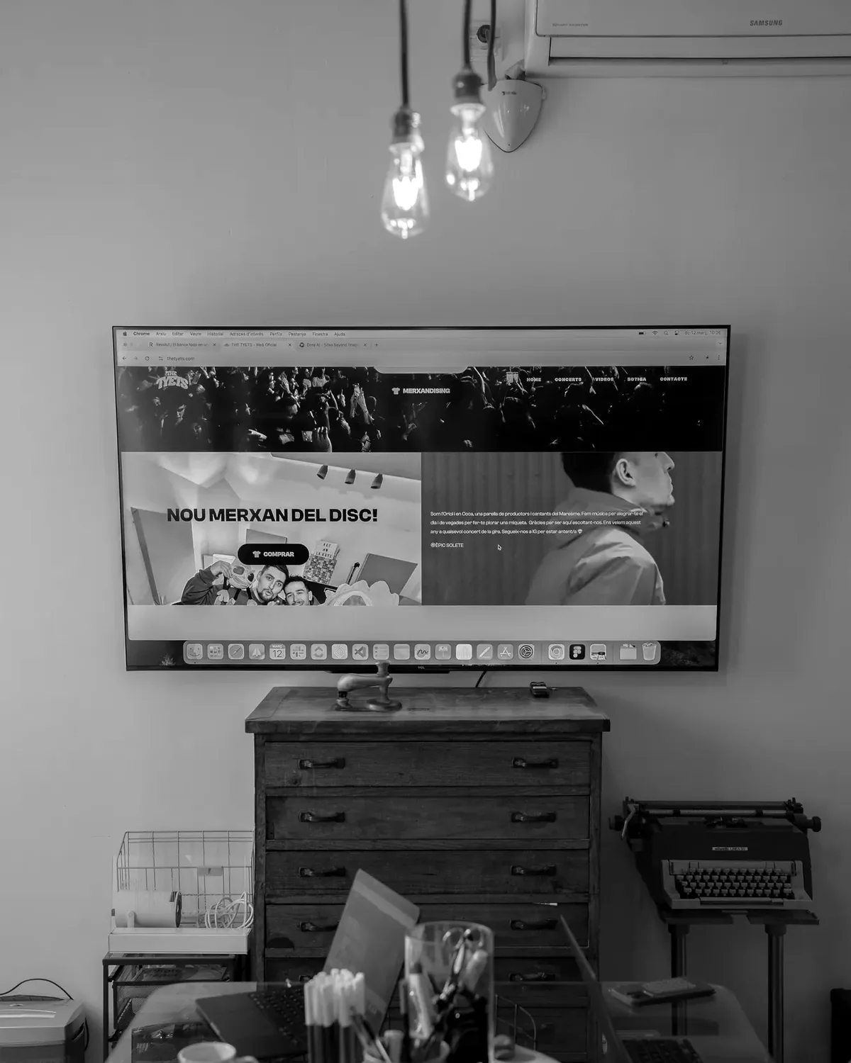 Una web oberta en una pantalla de l'estudi, amb la calaixera i la màquina d'escriure al davant.